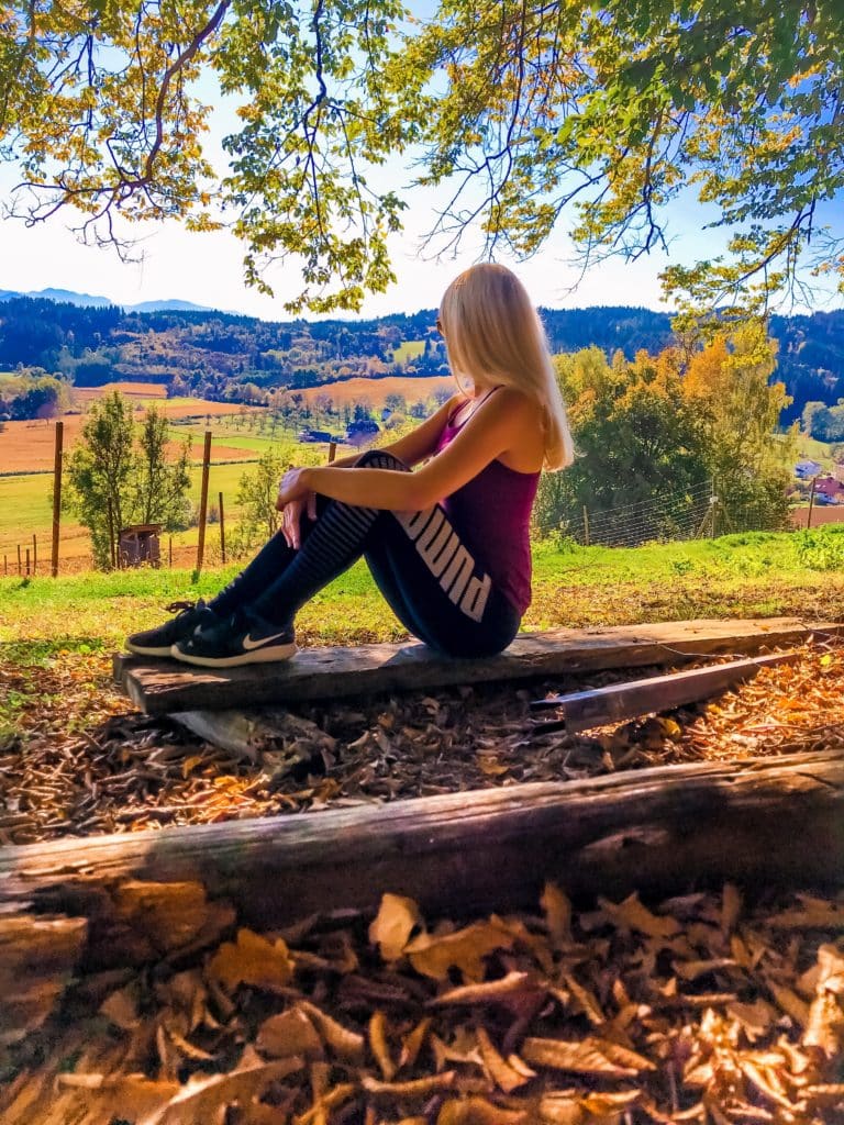 Sportlerin bei Sonnenuntergang die in der Wiese auf einem kleinen Berg sitzt und die Aussiht genießt. 