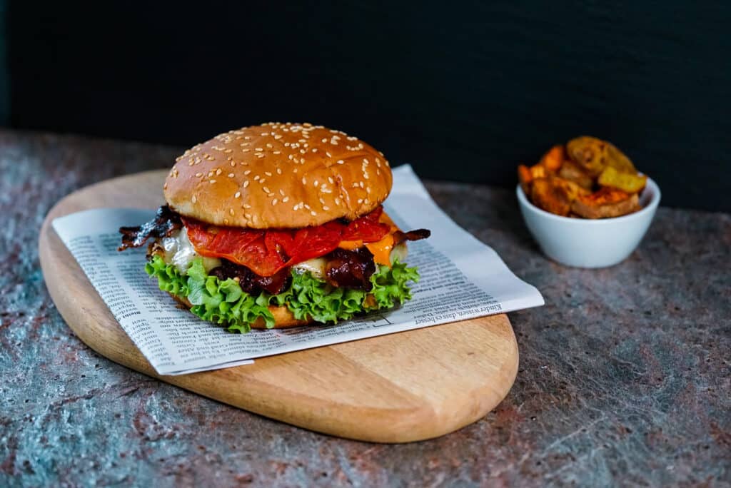 Selbstgemachter Burger vom Grill auf einem Holzbrett angerichtet 