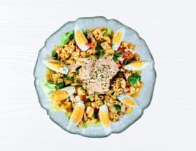 Gesunder Nudelsalat mit Hühnerfleisch und Gemüse angerichtet auf einem weißen Tisch. Der Salat ist in einer Glasschüssel angerichtet.