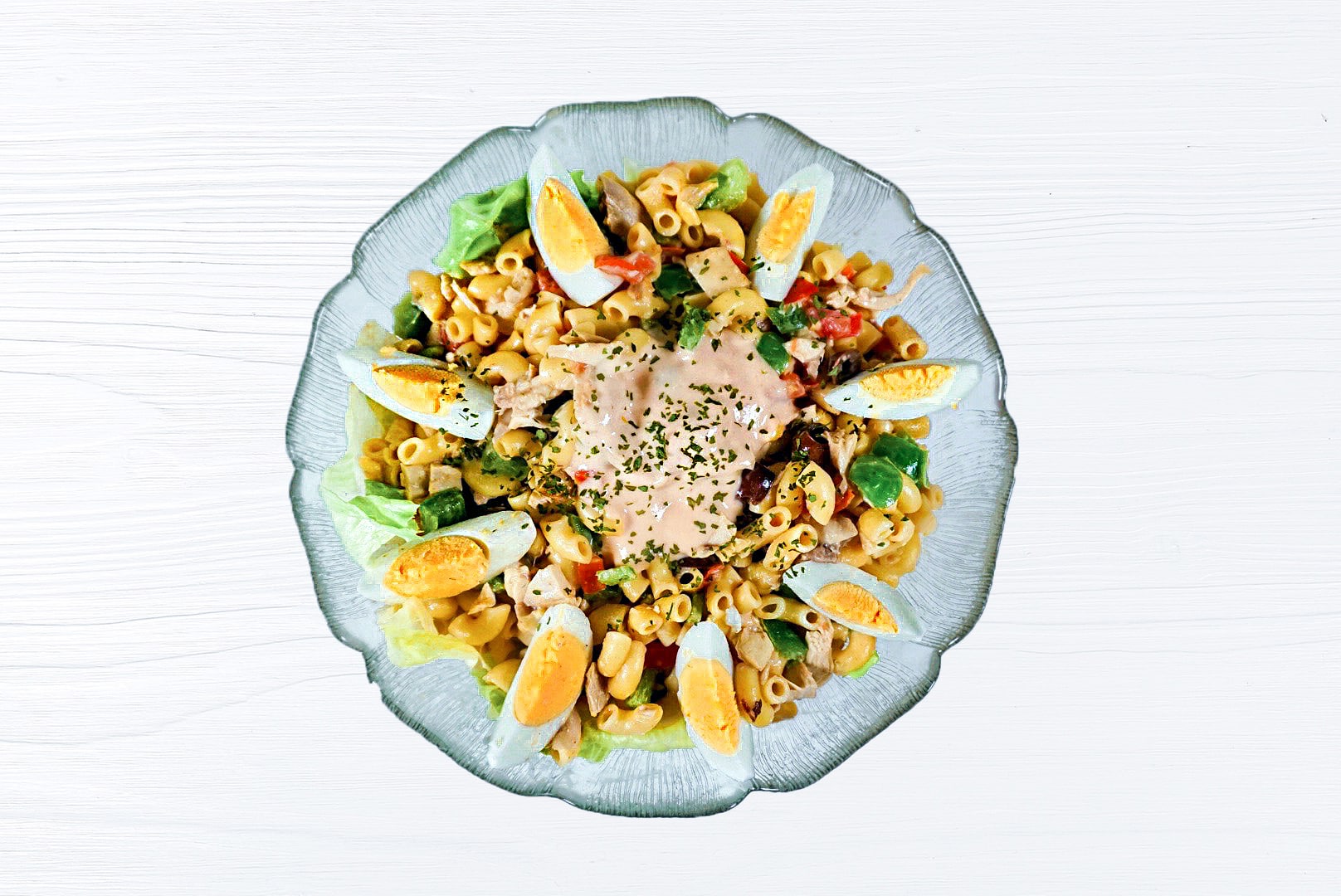 Gesunder Nudelsalat mit Hühnerfleisch und Gemüse angerichtet auf einem weißen Tisch. Der Salat ist in einer Glasschüssel angerichtet.