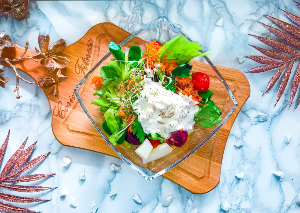 Bunter gemischter Salat in einer Glasschüssel auf einem Schneidebrett aus Holz serviert.