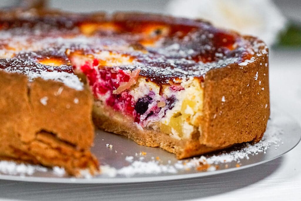 Angeschnittener gebackener Cheesecake mit Beeren auf einem weißen Tisch serviert. 