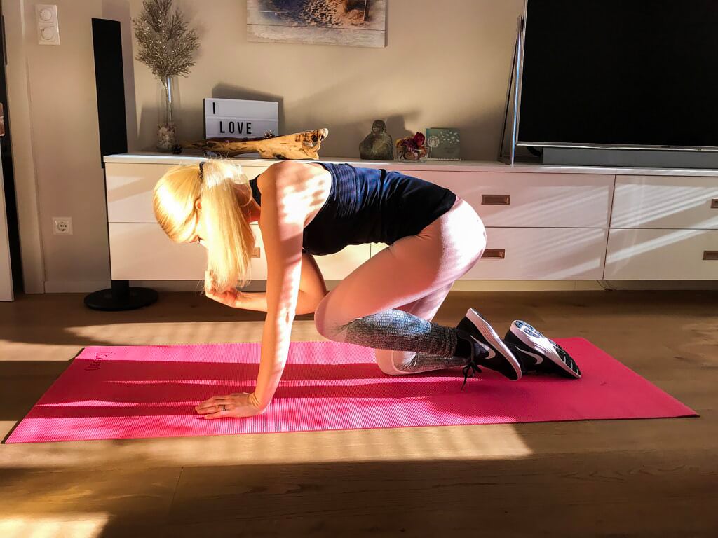 Fitnessgirl beim Homeworkout. Uebung Superman. Im Vierfueßlerstand rechten Arm und linkes Knie zusammen führen. Seite wieder wechseln zur Ausgangsposition. 